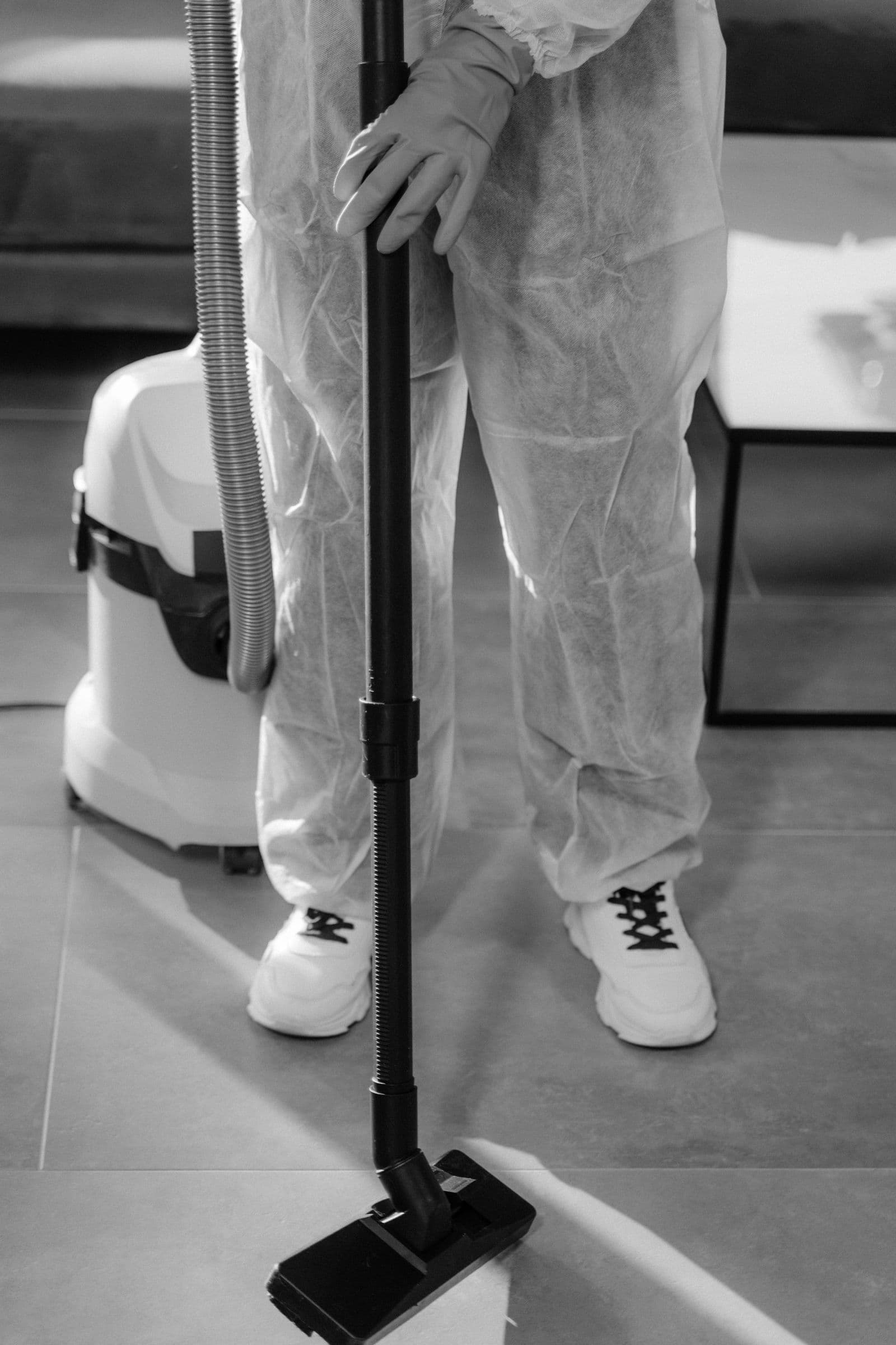 Restoration technician in protective coveralls extracting water from a floor with a wet vacuum